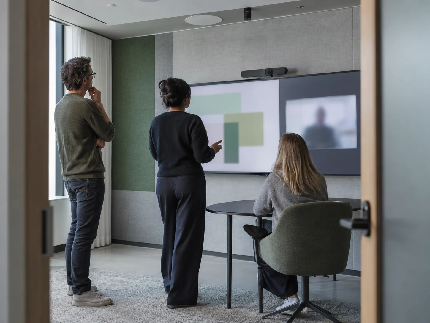 Three people work with a shared display in a meeting room.